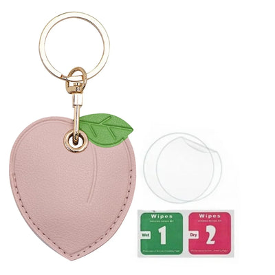 Peach-shaped pink leather AirTag keychain with green leaf, gold hardware, hand straps